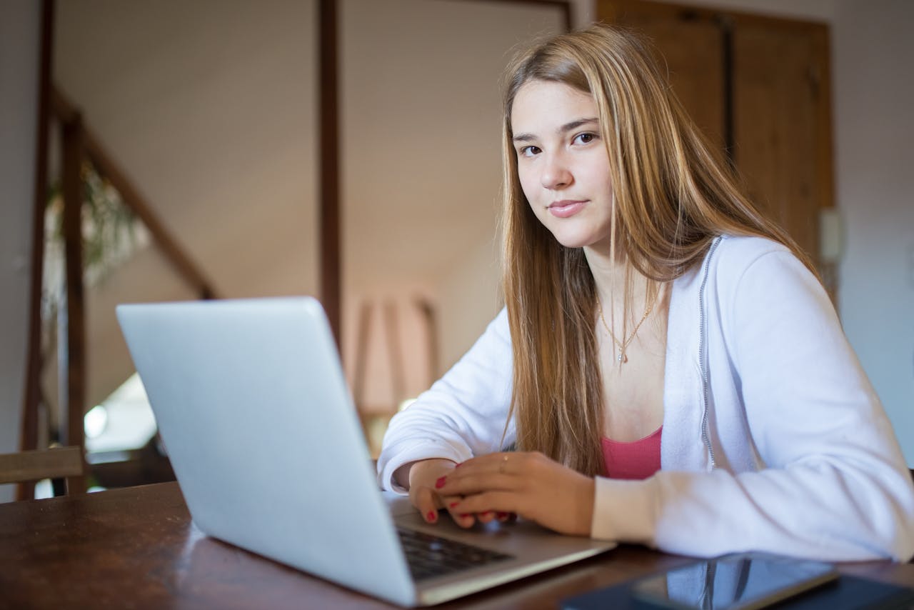 Confident young woman using a laptop while sitting at a wooden desk indoors.